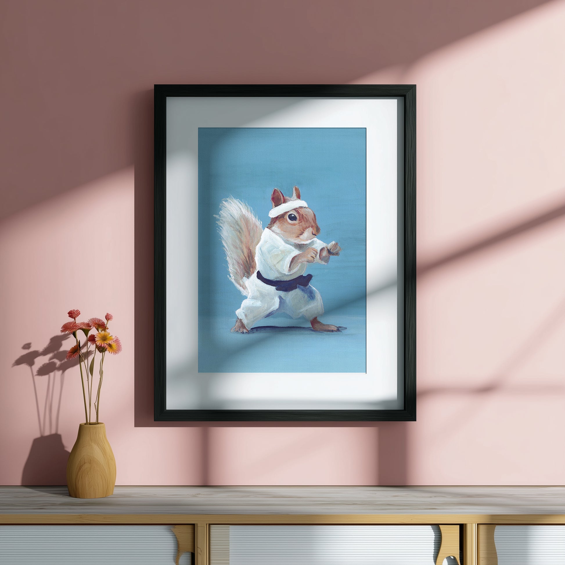 Framed artwork of a squirrel in a martial arts pose on a pink wall.